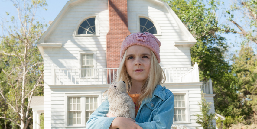 una bambina con uno zucchetto rosa e la giacca azzurra tiene in mano un peluche mentre sta fuori dalla sua casa tutta bianca - nerdface